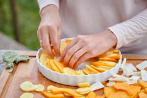Vorbereitung eines Gratins von Kartoffeln, Kürbis und Topinambur, Anordnen der aufgeschnittenen Zutaten in einer gebutterten Backform Vorbereitung eines Gratins von Kartoffeln, Kürbis und Topinambur, Anordnen der aufgeschnittenen Zutaten in einer gebutterten Backform